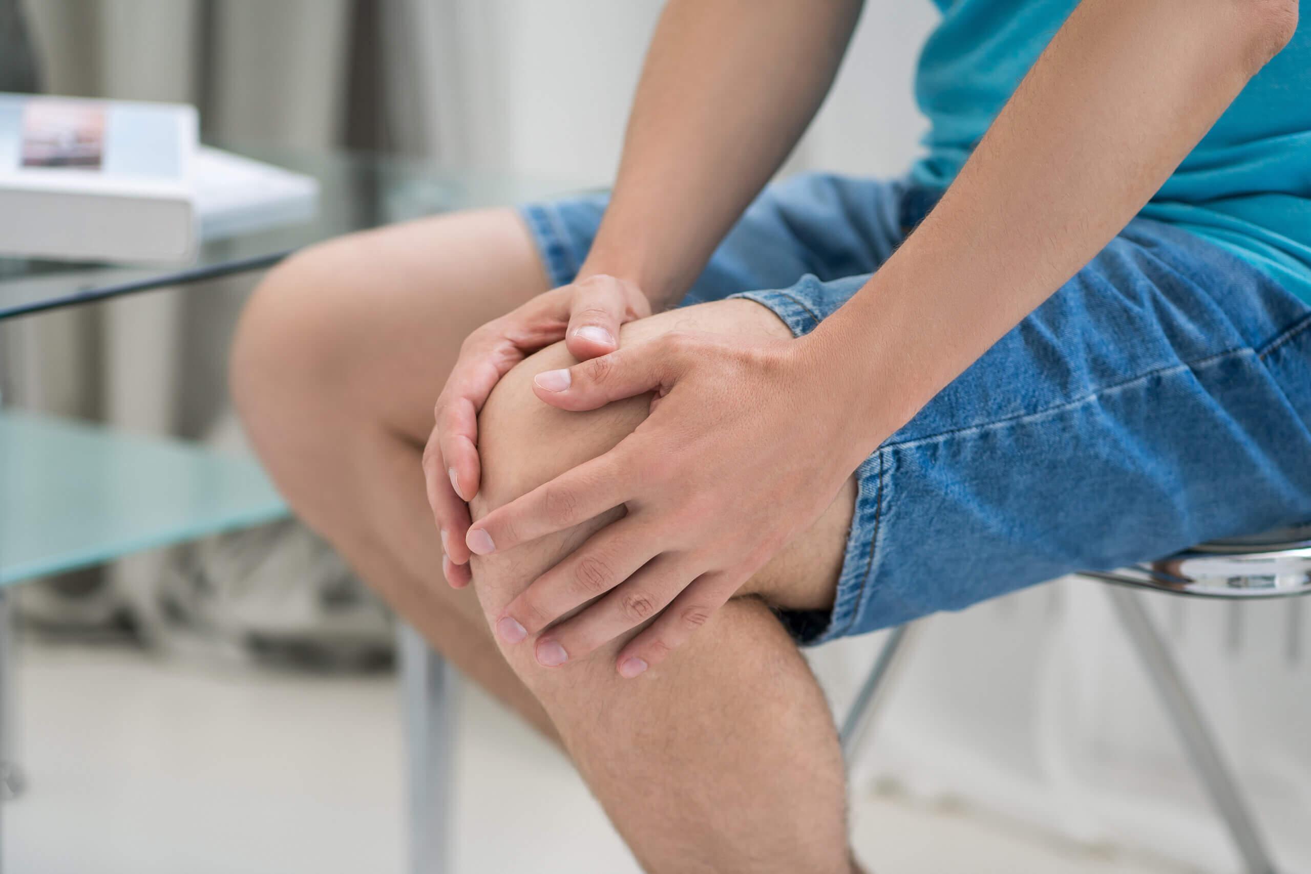 Knieschmerzen, Mann leidet unter Schmerzen und macht zu Hause Selbstmassage, selbstberuhigende Massage