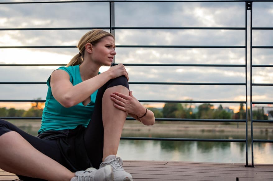 Junge FRau sitzt am Boden und hält sich am Knie
