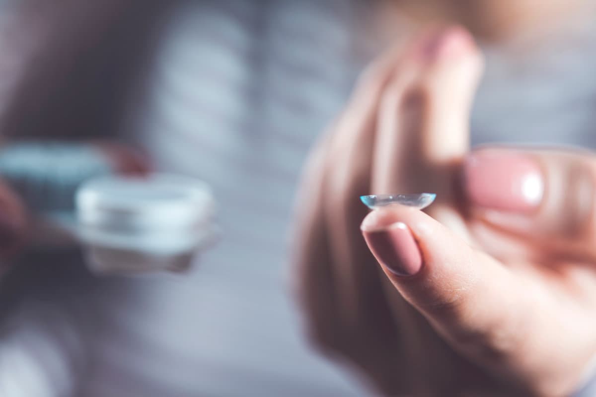 Woman holding contact lens on gray background