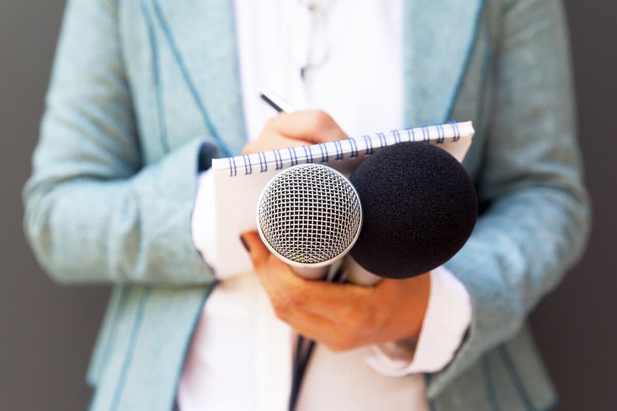 Reporterin bei Pressekonferenz, Notizen machen, Mikrofon halten