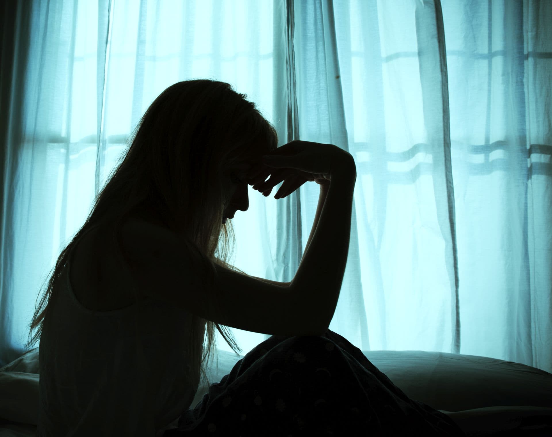 Silhouette of woman sitting in bed by window