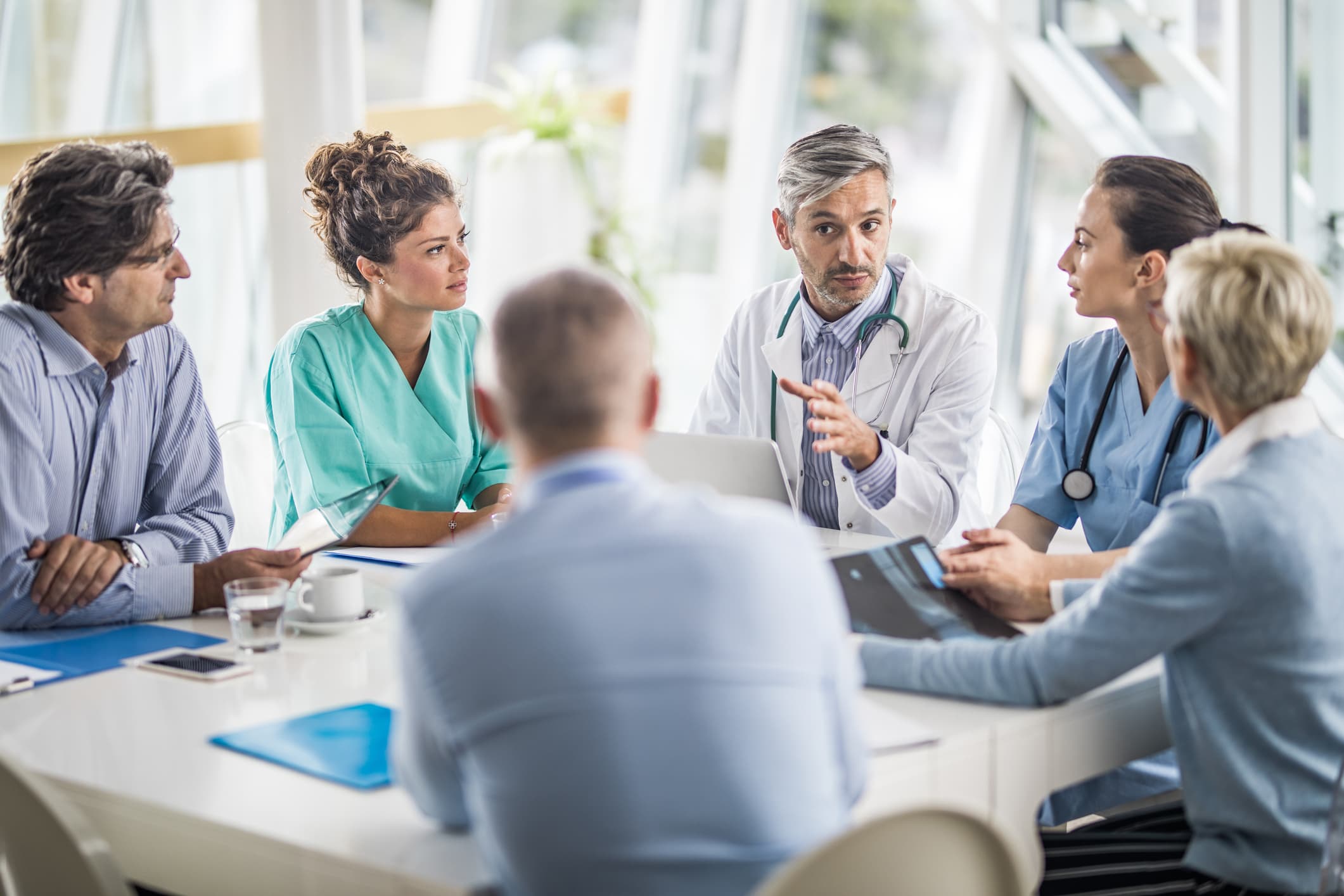 Männlicher Arzt und seine Kolleginnen sprechen mit einem Team von Geschäftsleuten bei einem Treffen im Krankenhaus.