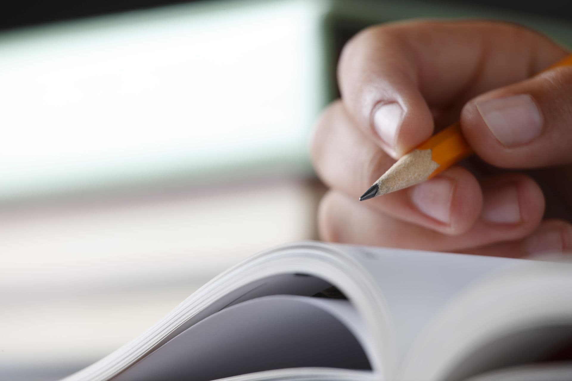 A closeup of a teenager holding a pencil while doing homework. Shot with shallow depth of field.