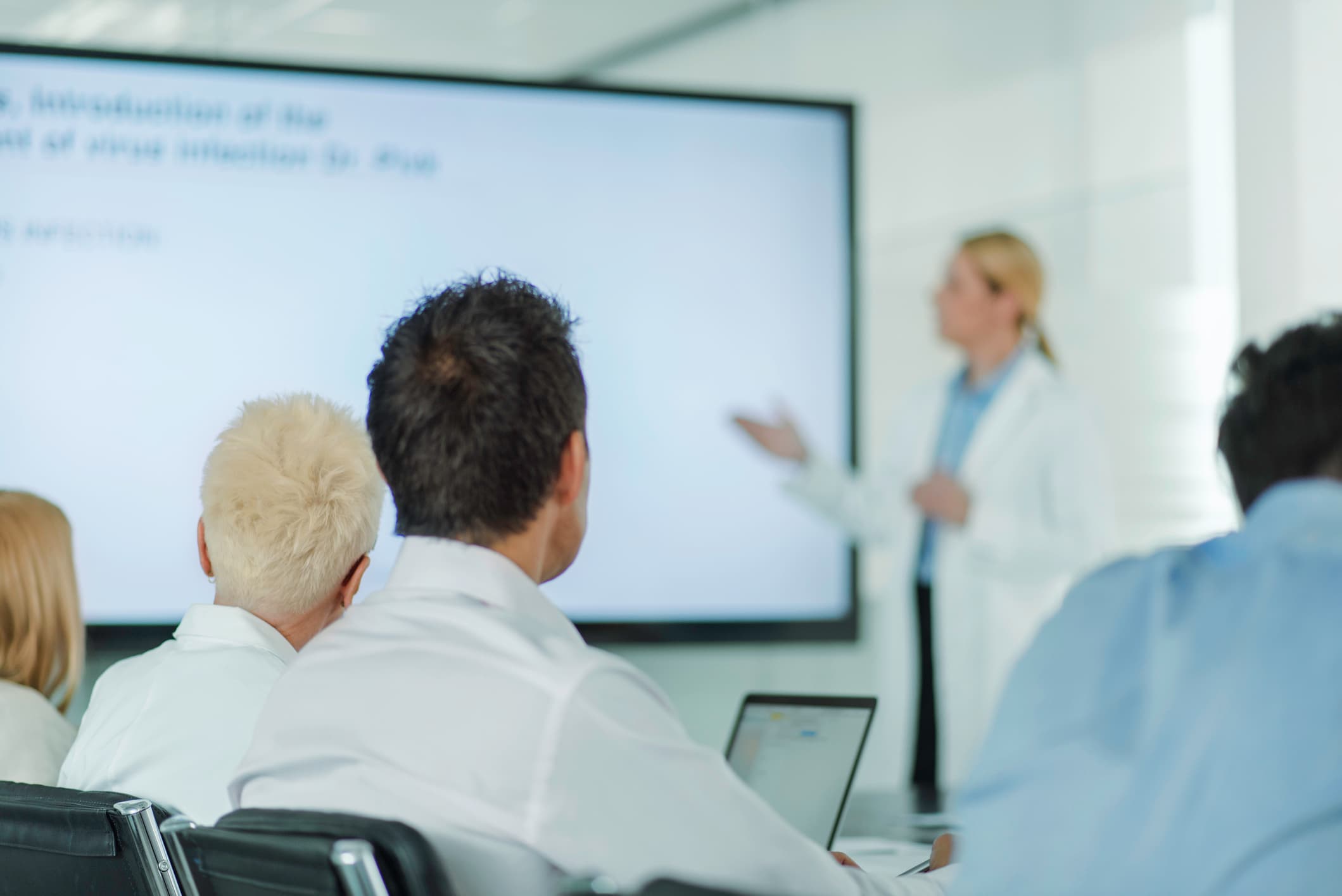 Gruppe von Ärzten, Forschern und medizinischem Personal, die der Präsentation eines Forschers zuhören.