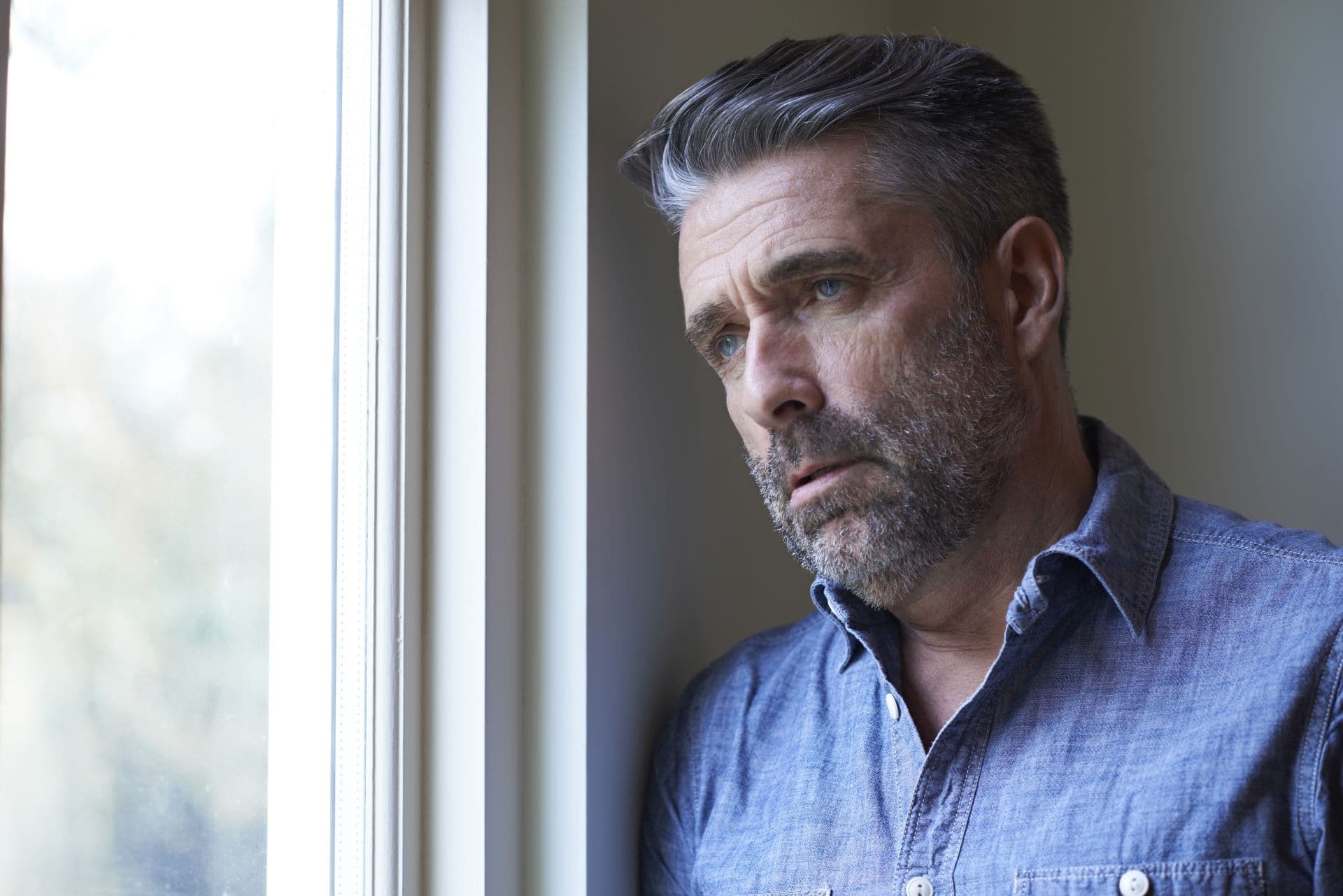 Mature Man Suffering From Depression Looking Out Of Window