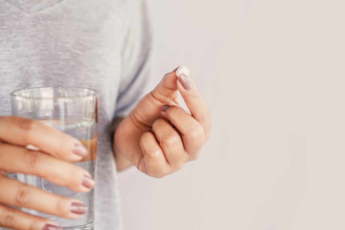 closeup woman hand taking pill with glass of water, healthcare and medical concept