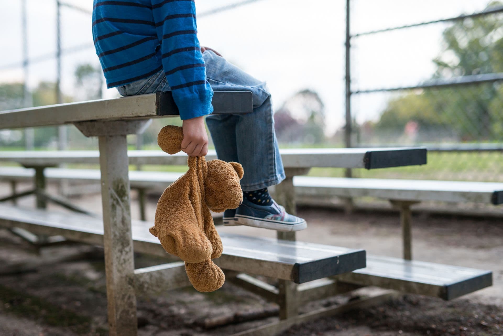 Junge, der allein auf Tribünen sitzt und Teddybär hält.