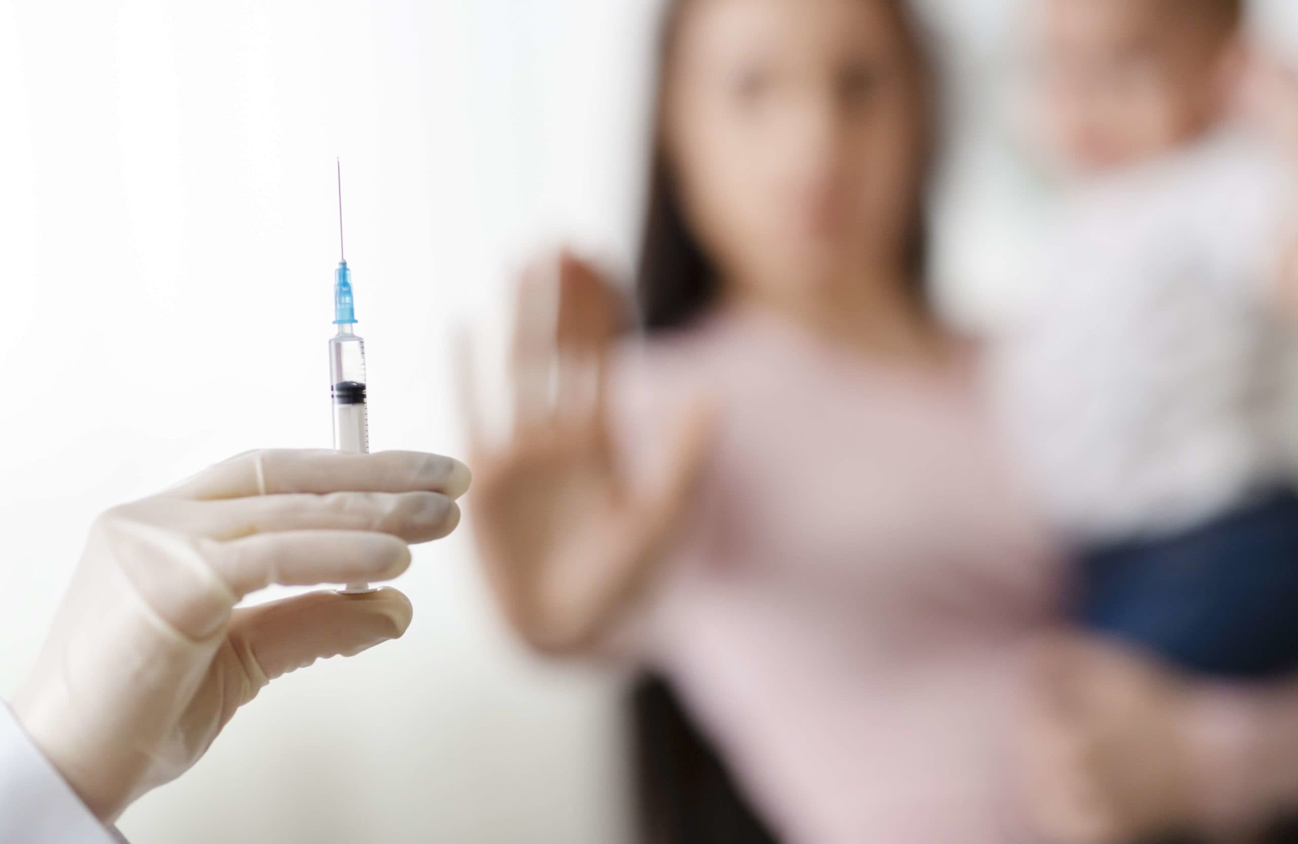 Stoppen Sie die Impfung von Kindern. Mutter hält Baby und lehnt Arzt mit Spritze ab, selektiver Fokus