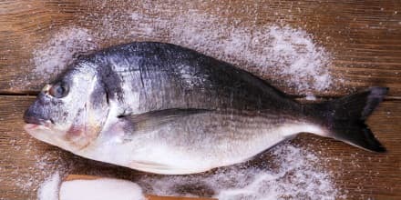 Fresh fish and salt in spoon on wooden background