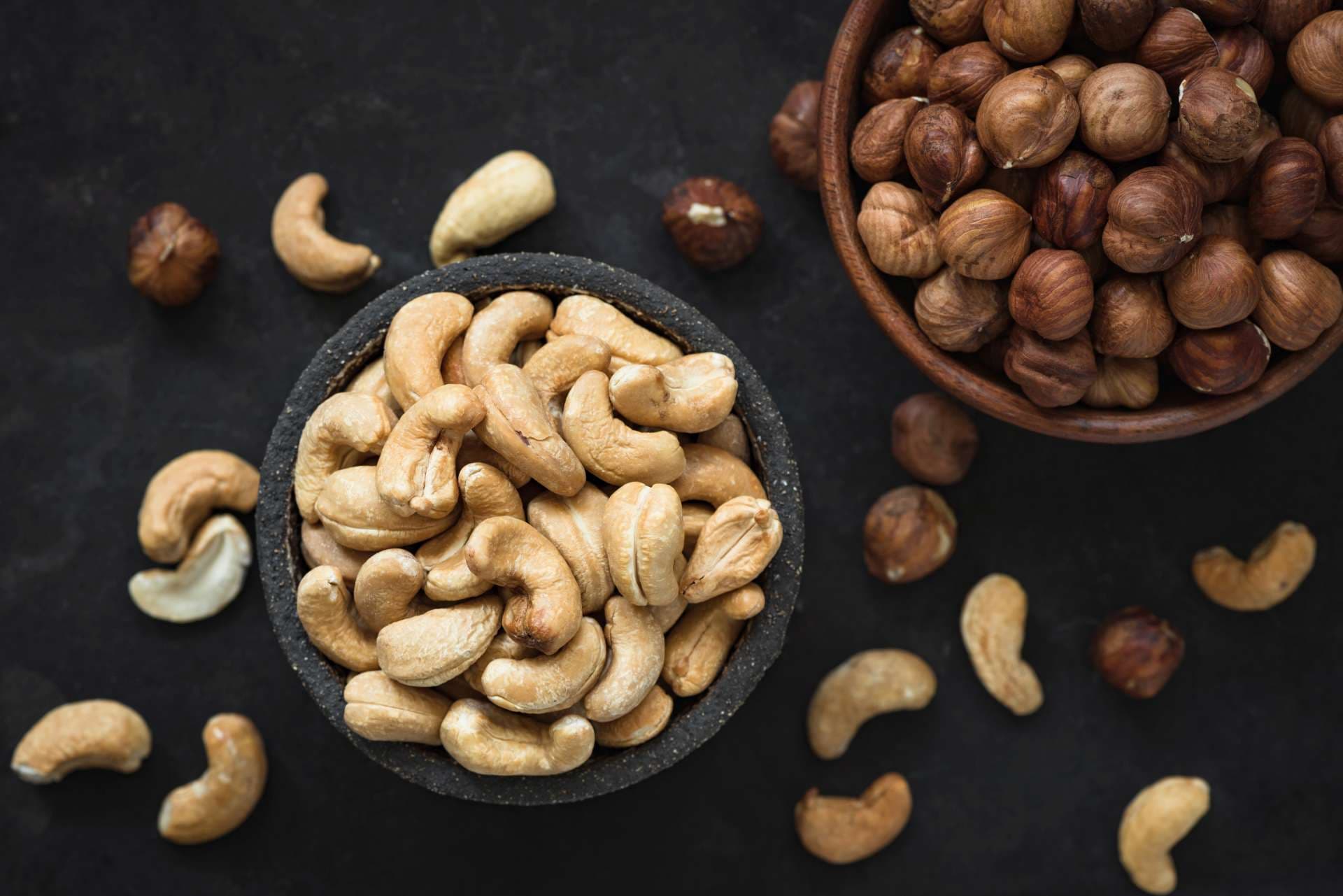Gemischte Nüsse auf schwarzem Betonhintergrund, Draufsicht. Cashewnüsse und Haselnüsse in der Schüssel