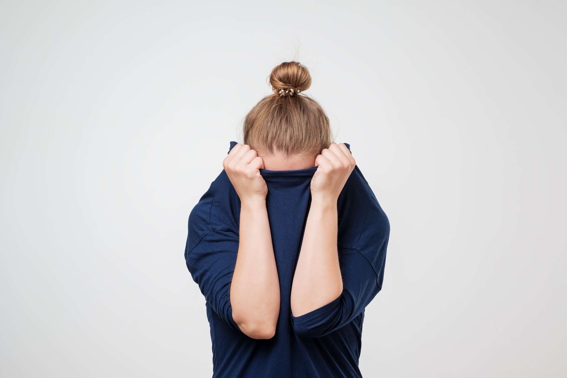 European woman hiding face under the clothes. She is oulling sweater on her head. Depressed emotion. Wish to be alone.