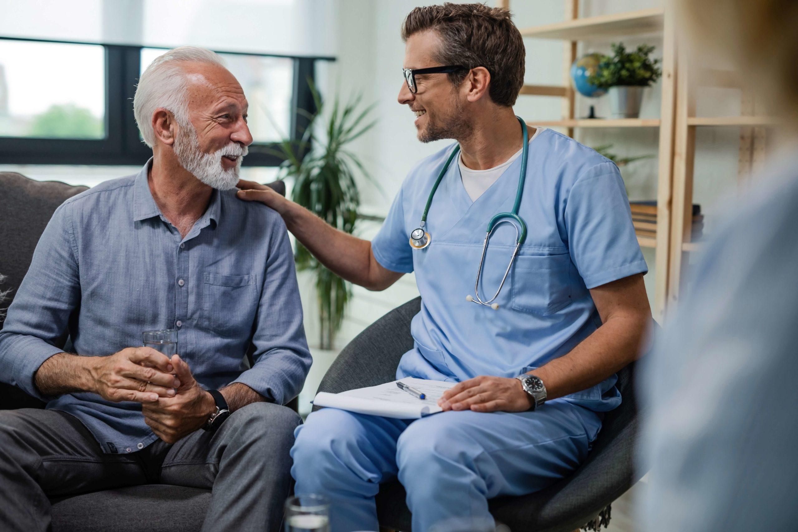 Glücklicher Arzt, der mit einem älteren männlichen Patienten spricht, während er bei einem Hausbesuch ist.