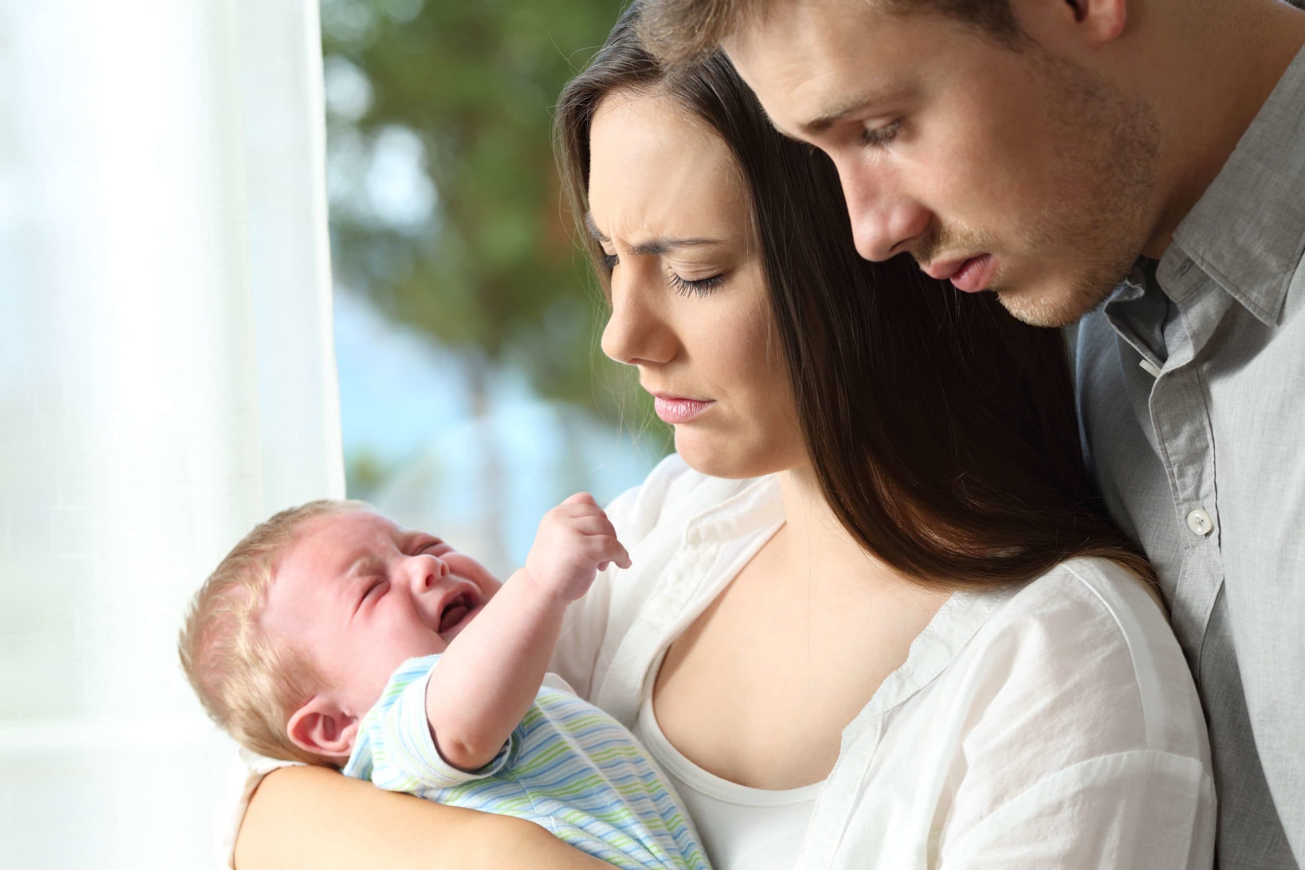 Müde, verzweifelte Eltern, die ihr Baby zu Hause verzweifelt weinend halten