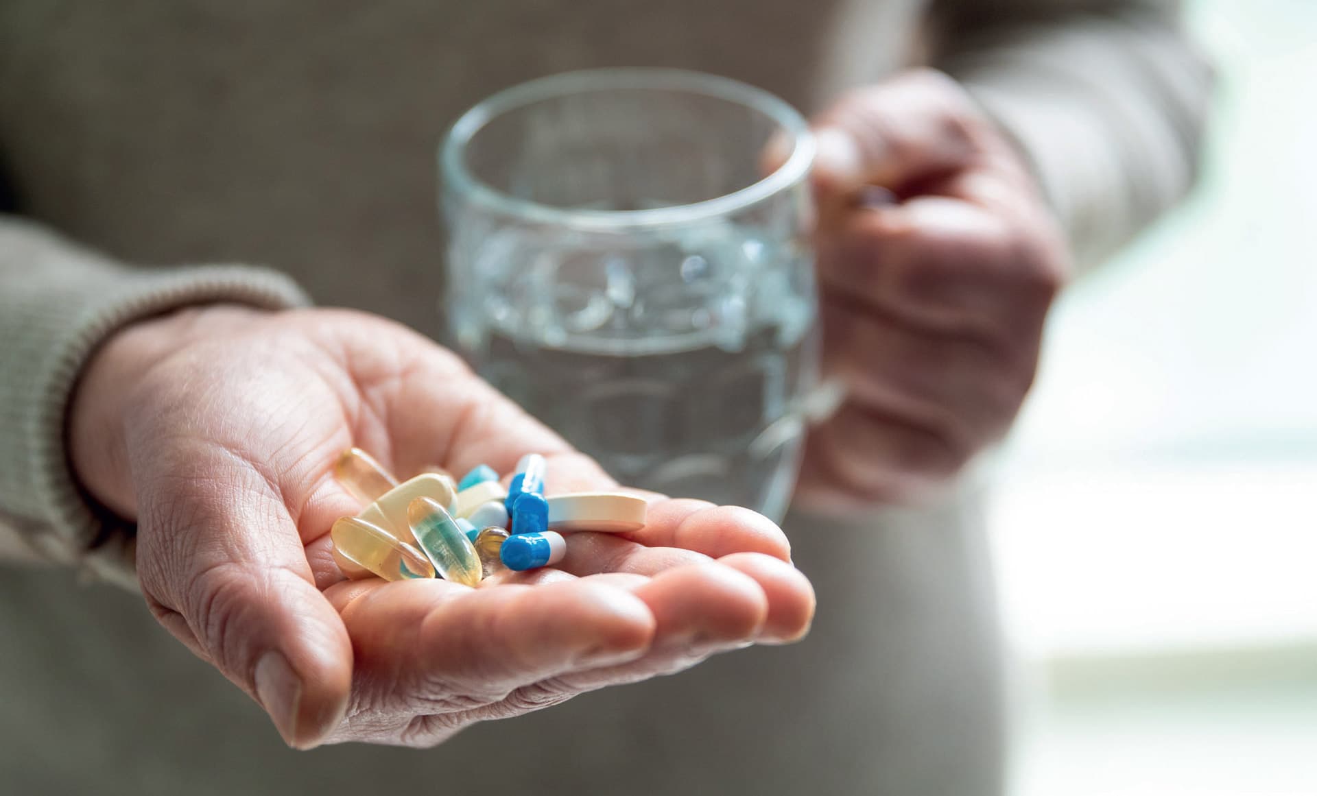 Eine Hand die mehrere Tabletten hält, während die andere Hand ein Glas Wasser hält.