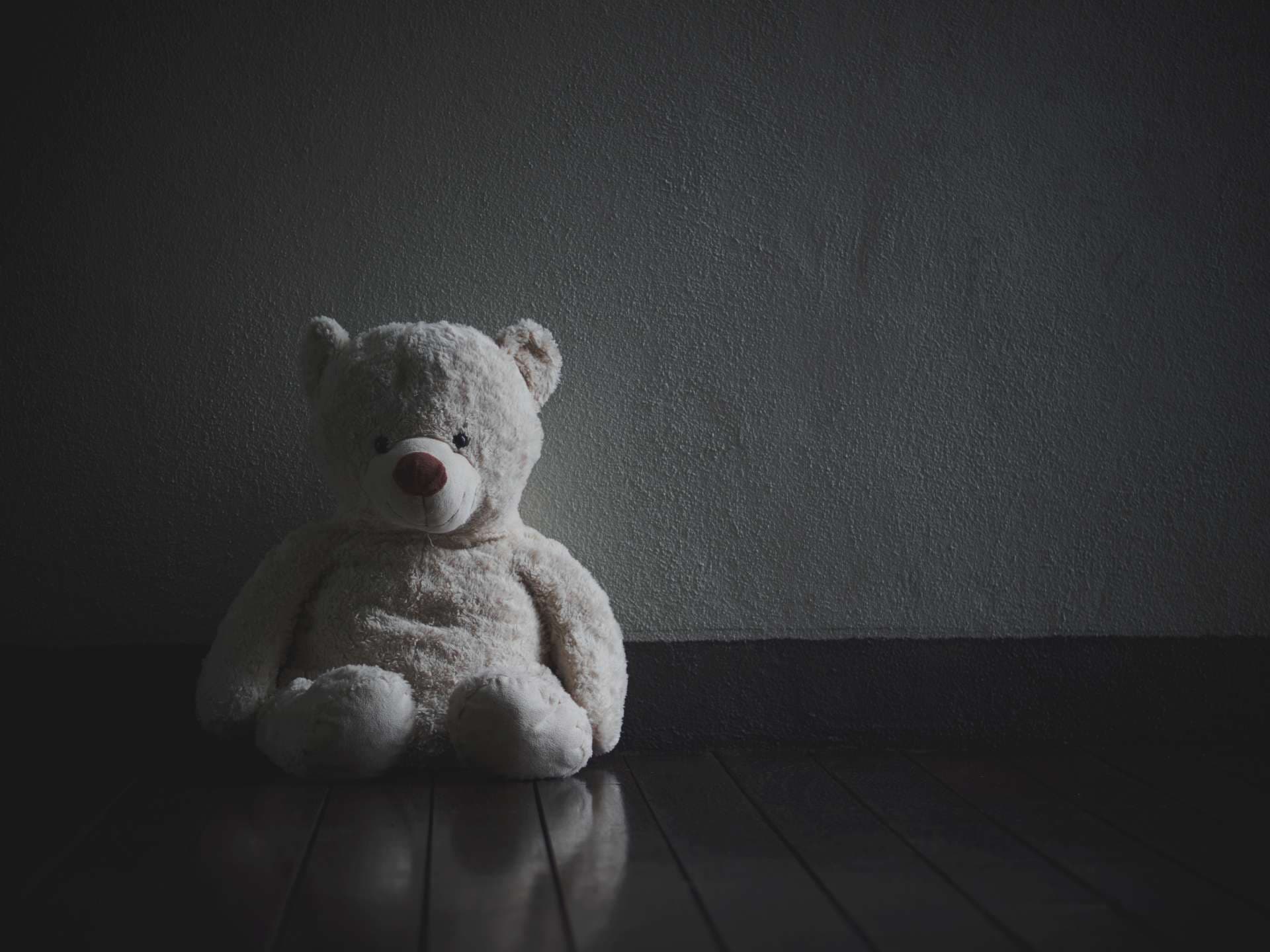 Einsamer Teddybär, der im dunklen Raum sitzt (Konzept über die Liebe)