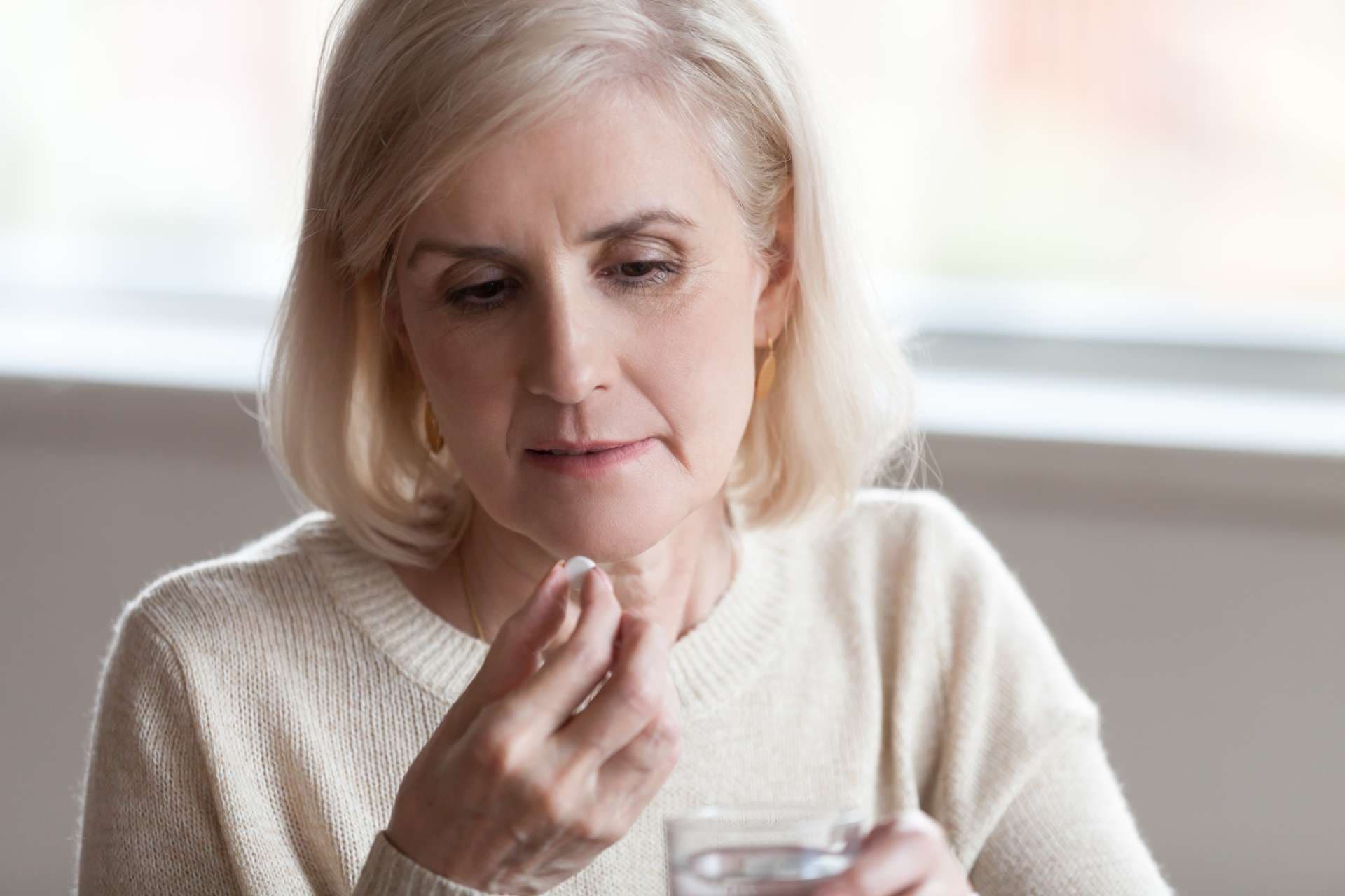 Gealterte Frau, die Glas Wasser und Pille hält