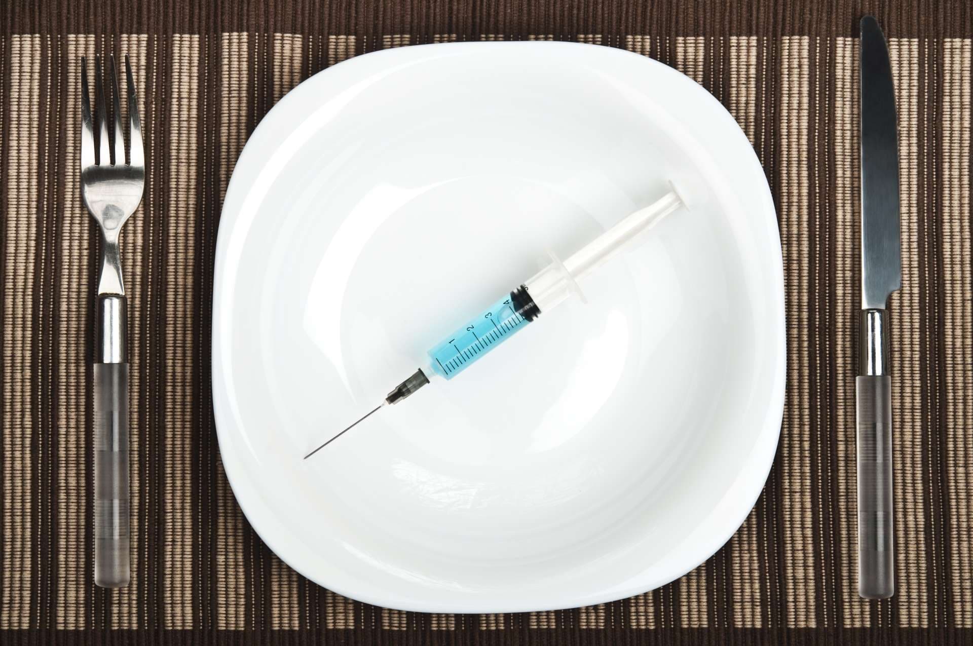 Spritze mit Gabel und Messer auf Teller