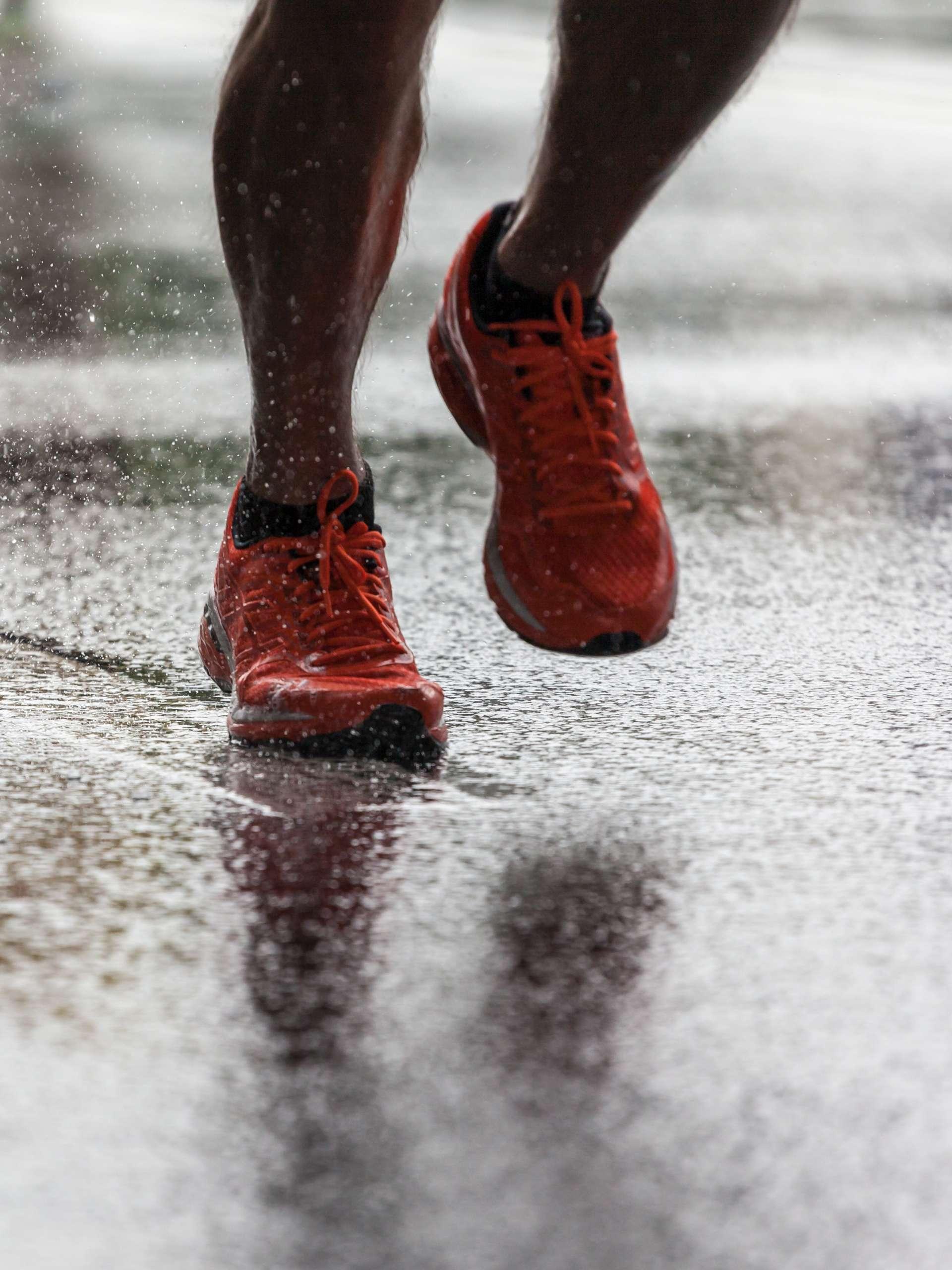 Nahaufnahme von Sportschuhen eines Athleten, der auf einem nassen Asphalt läuft. Spritzwasser unter den Füßen. Training im Regen.