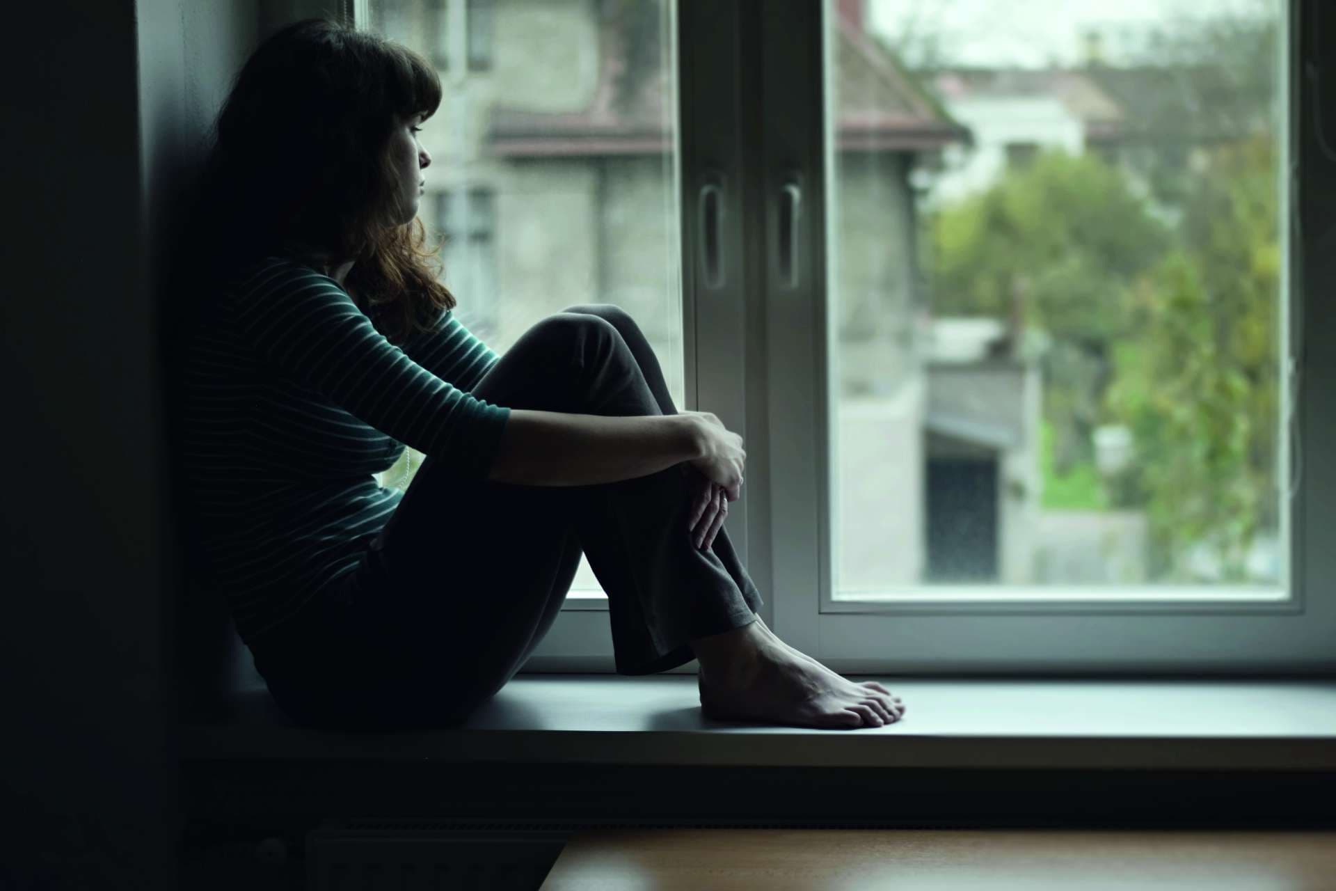 Traurige junge Frau, die am Fenster sitzt