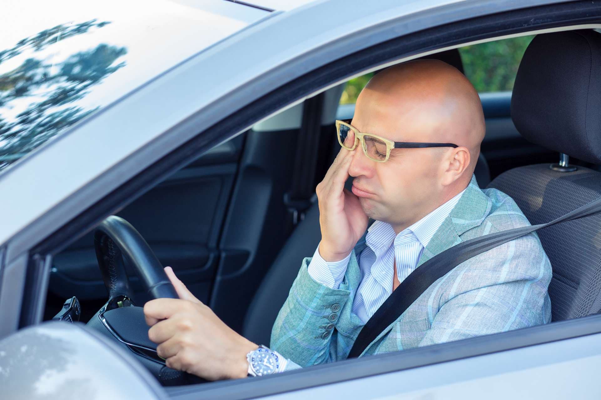 Schläfriger, müder, erschöpfter junger Mann, der nach einer langen Autostunde sein Auto im Verkehr fährt.