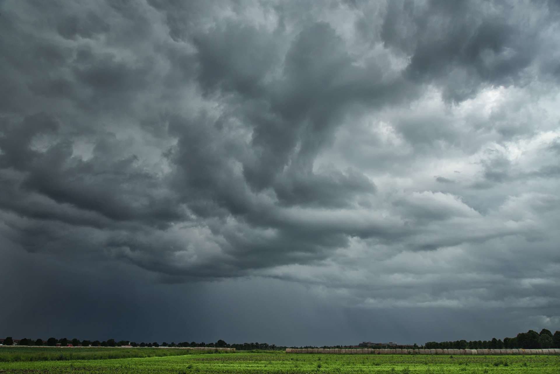 Düstere, bedrohliche Wolken ziehen über eine sommerliche, ländliche Landschaft und bringen Starkregen mit Gewittern.