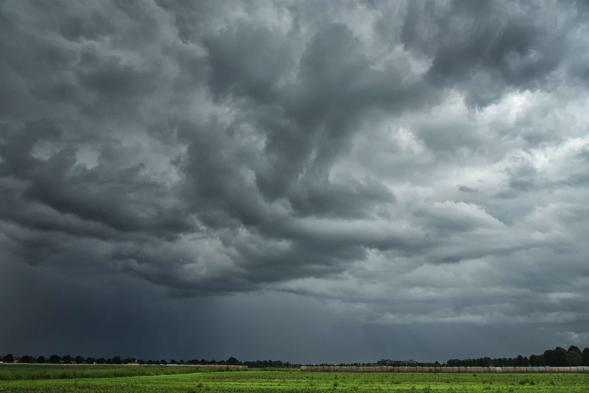 Düstere, bedrohliche Wolken ziehen über eine sommerliche, ländliche Landschaft und bringen Starkregen mit Gewittern.