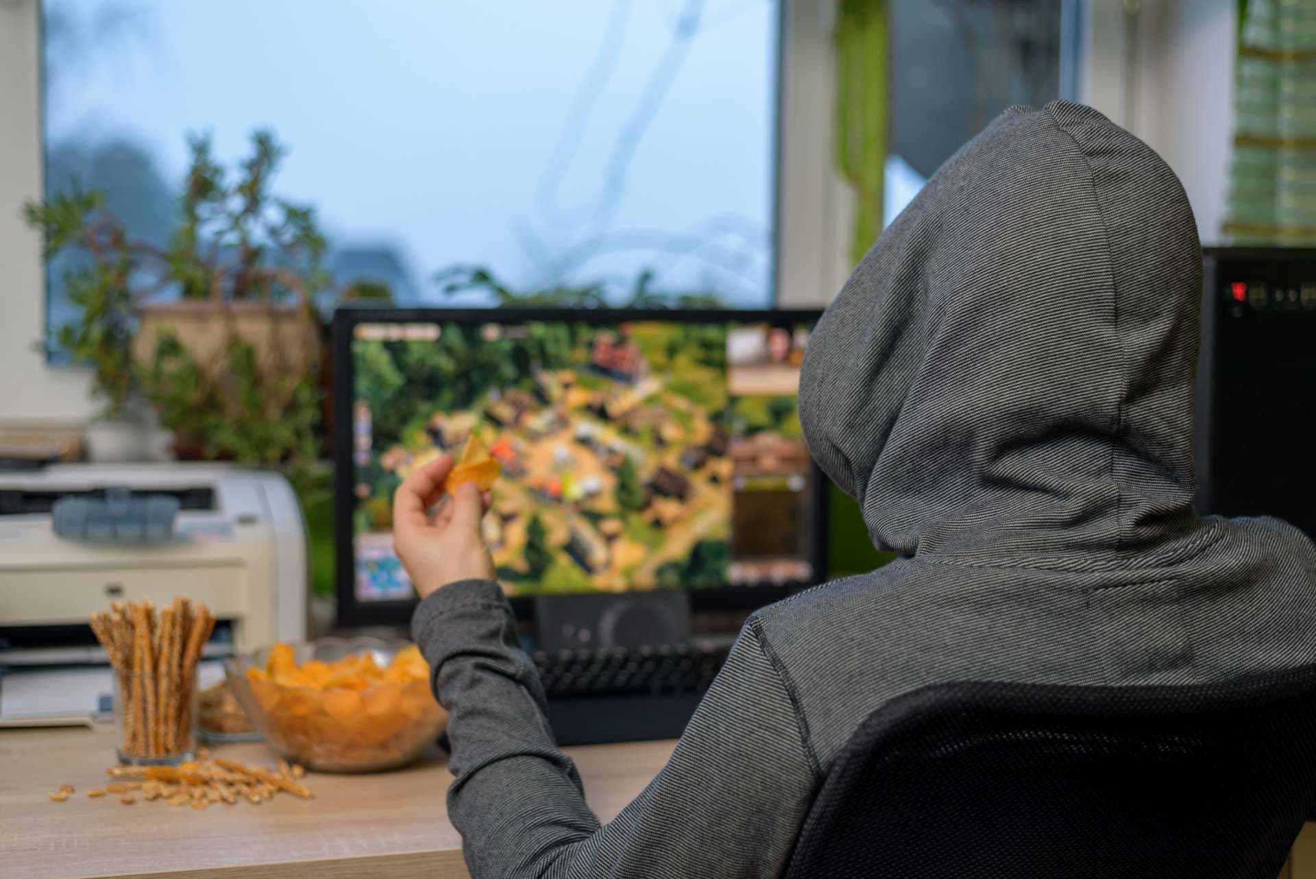 männlicher Spieler, der ein Strategiespiel auf dem Computer spielt und Snacks isst