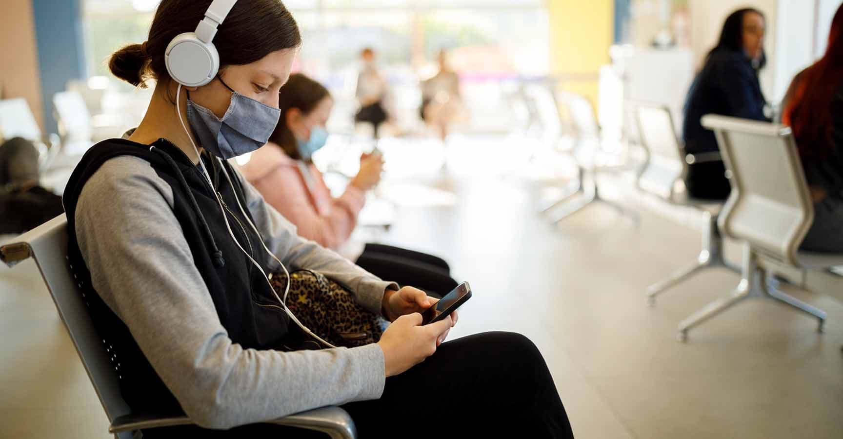 Kids with face protective mask using mobile phone while waiting at airport