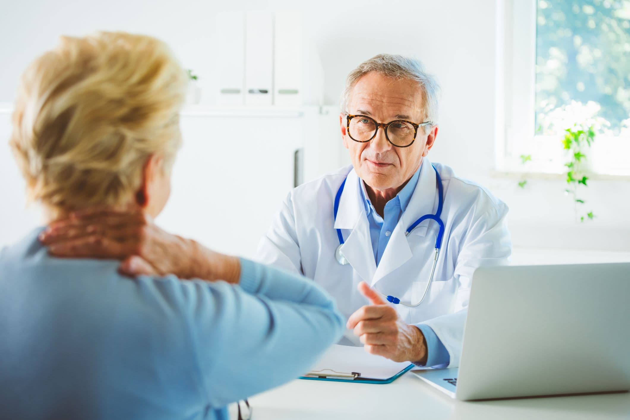 Senior Gesundheitspersonal im Gespräch mit Patientin im Krankenzimmer. Doktor, der der älteren Frau zuhört, die Rückenschmerzen hat.