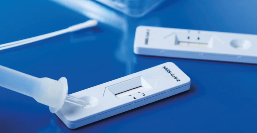 einige Covid-19-Antigen-Schnelltestkits mit den diagnostischen Testgeräten und einigen Nasopharynxabstrichen auf einer blauen Oberfläche