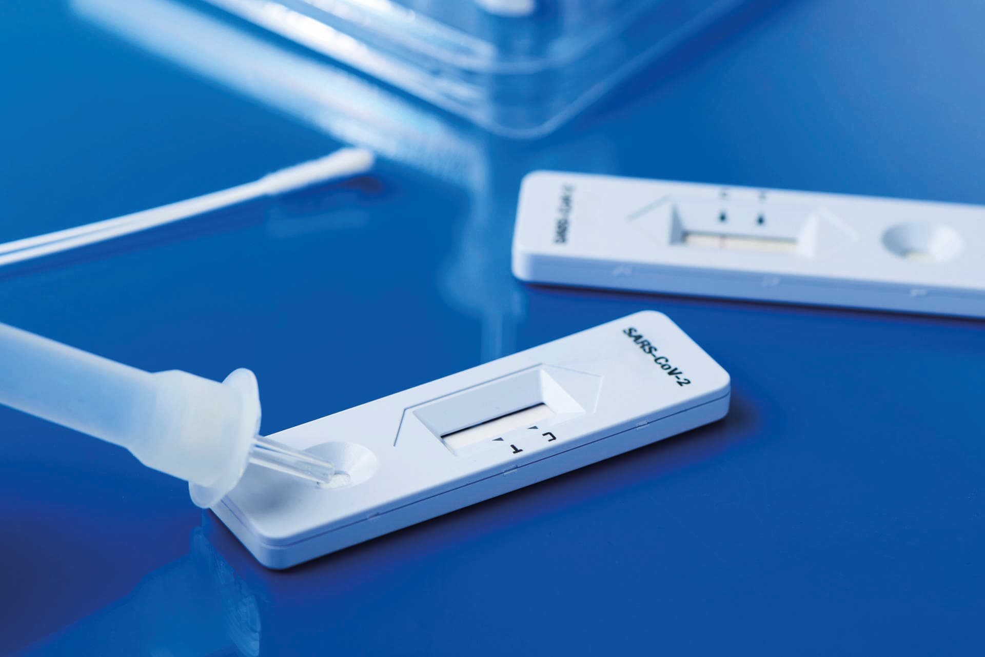 einige Covid-19-Antigen-Schnelltestkits mit den diagnostischen Testgeräten und einigen Nasopharynxabstrichen auf einer blauen Oberfläche