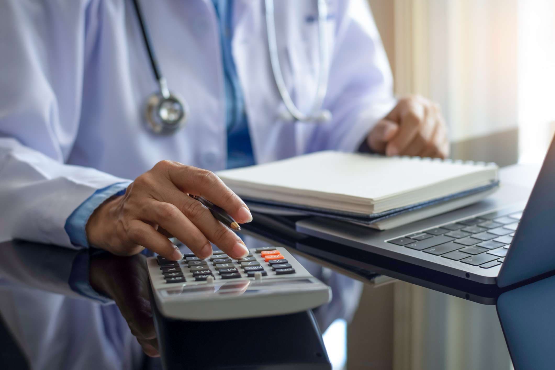 Ärztin mit Taschenrechner und Notebook am Schreibtisch im modernen Büro in der Klinik oder im Krankenhaus