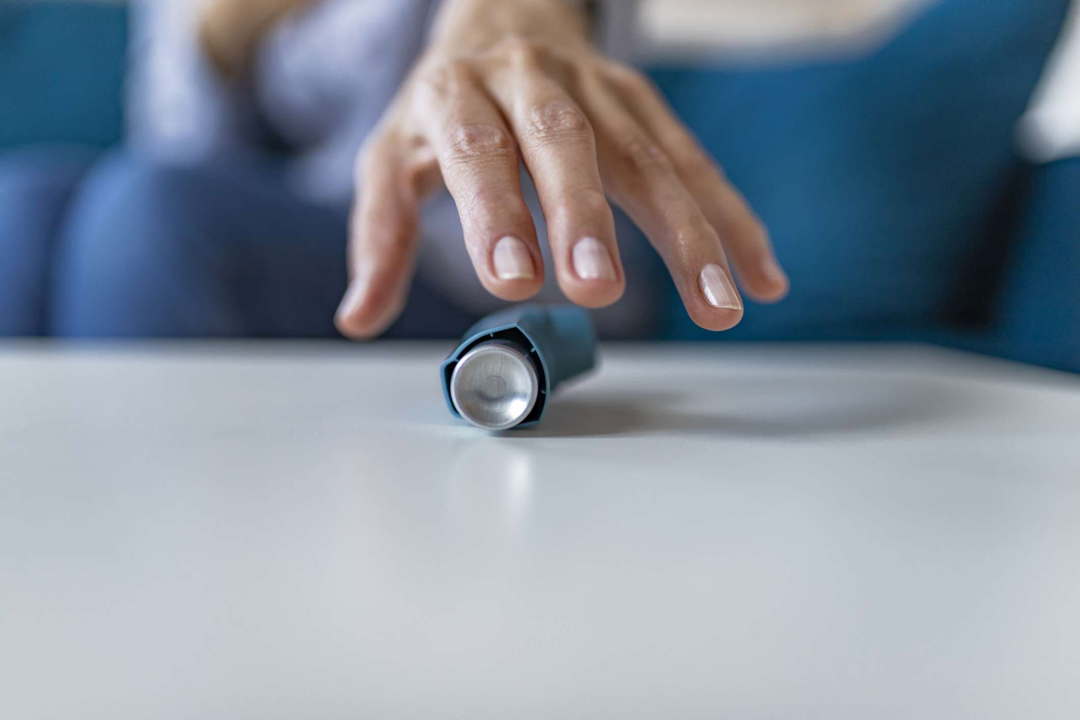 Woman Hand Reaching Inhaler Because She Suffering From Asthma Attack Sitting on a Couch in the Living Room at Home.