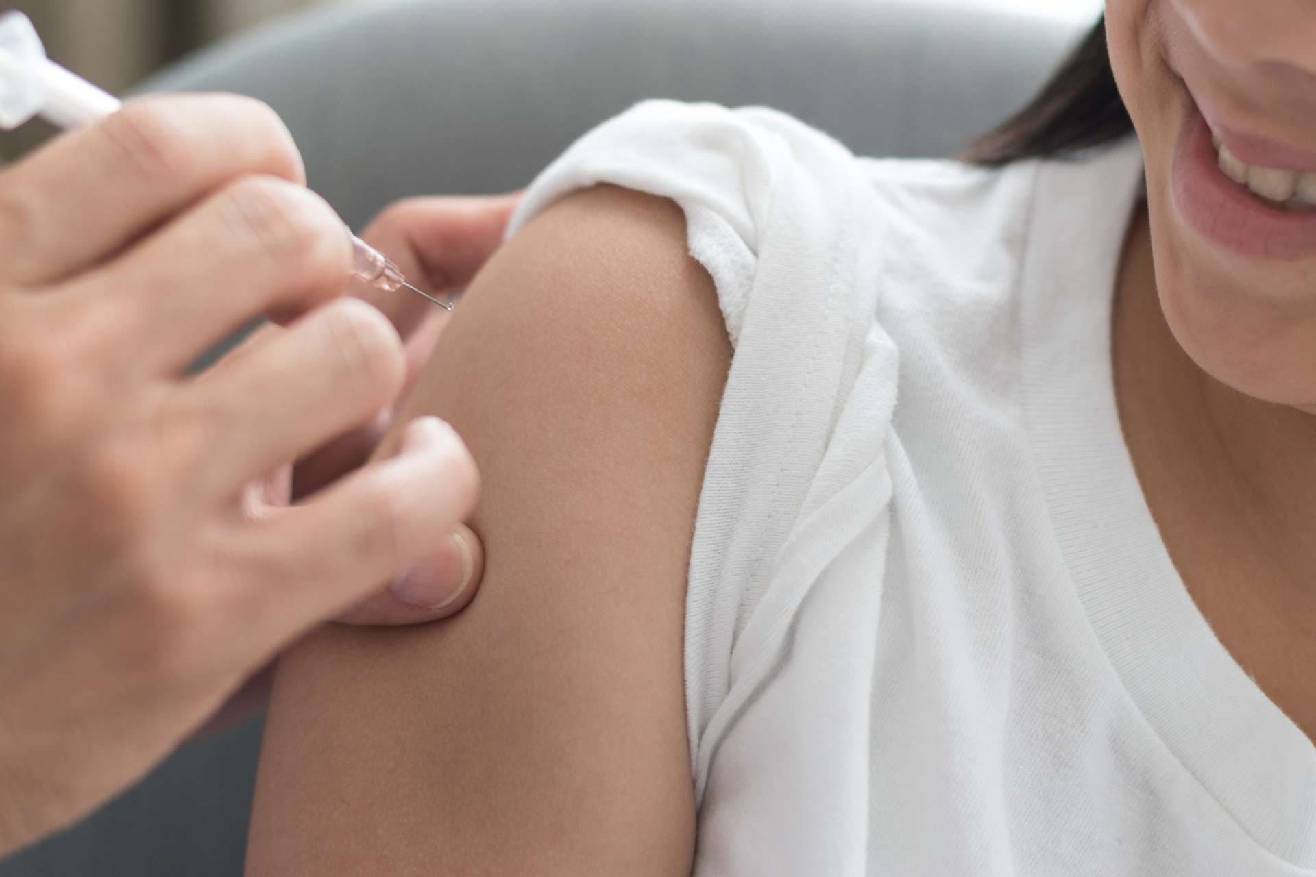 Weltimpfwoche und Konzept des Internationalen HPV-Sensibilisierungstages. Starkes glückliches gesundes Asienkindmädchen, das lächelt, Impfung gegen Influenza oder Grippeimpfung oder HPV-Prävention mit der Hand des Arztes Kinderarzt zu bekommen, die medizinische Spritze im Krankenhaus hält