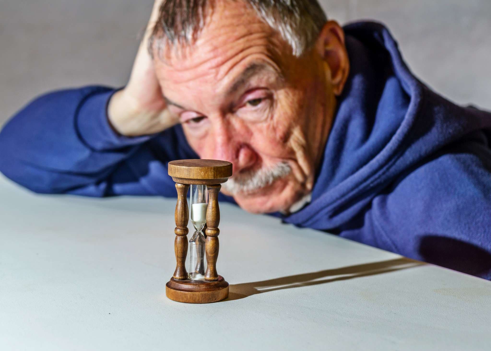 Älterer Mann, der beobachtet, wie eine Zeit vergeht, während Sand durch eine Sanduhr fällt