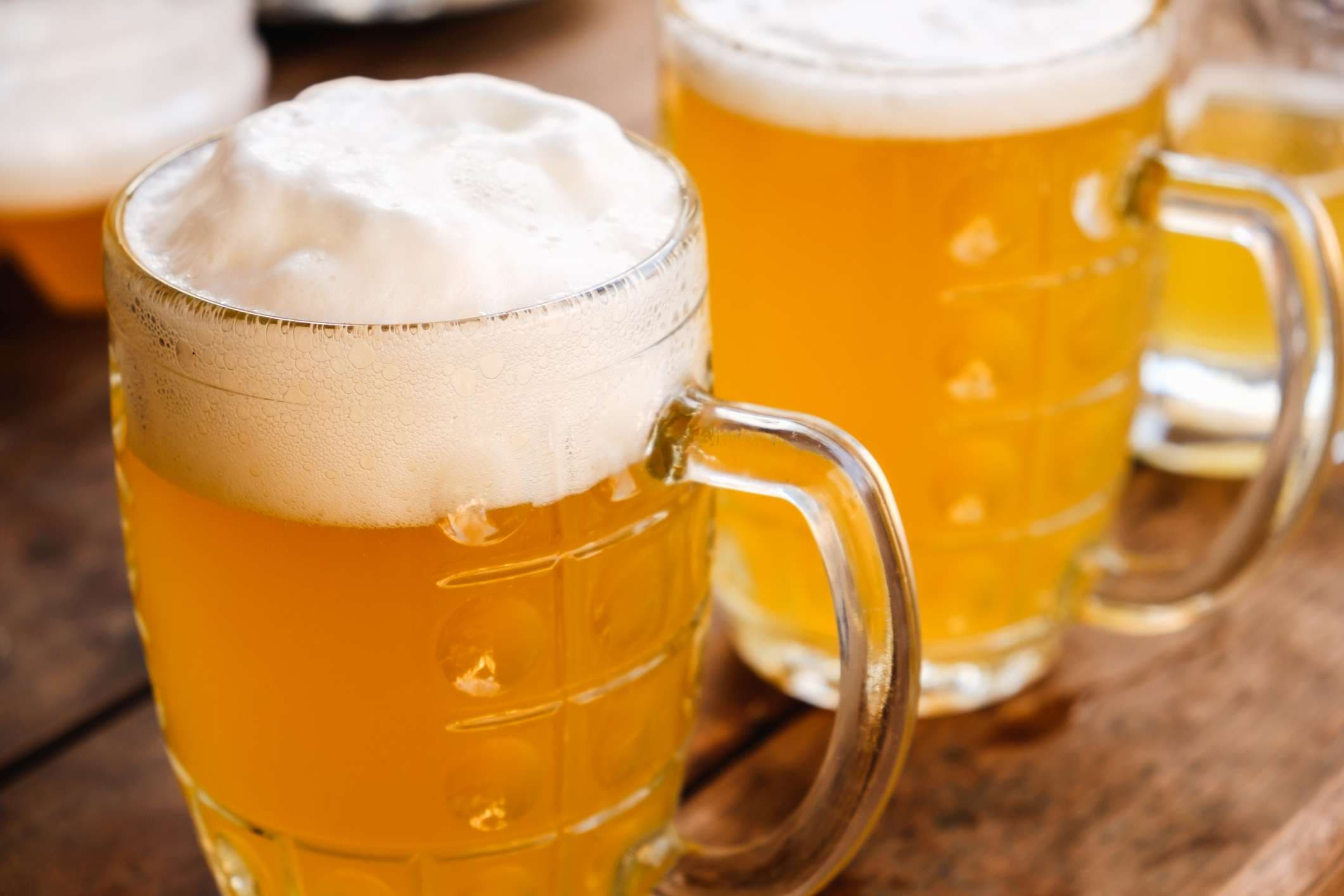 Nahaufnahme zwei kalte Biere mit Schaum und Wassertropfen auf altem Holztisch im Freien mit Sonnenstrahl