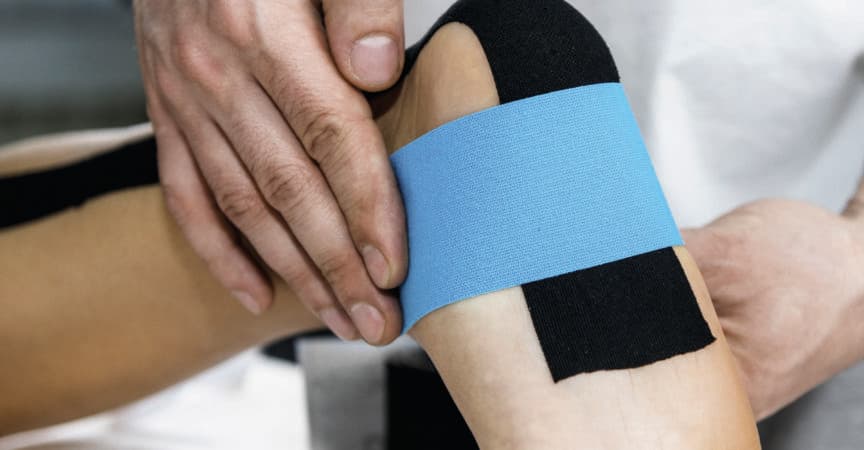 Physiotherapeut legt Tape am Fuß des Patienten an