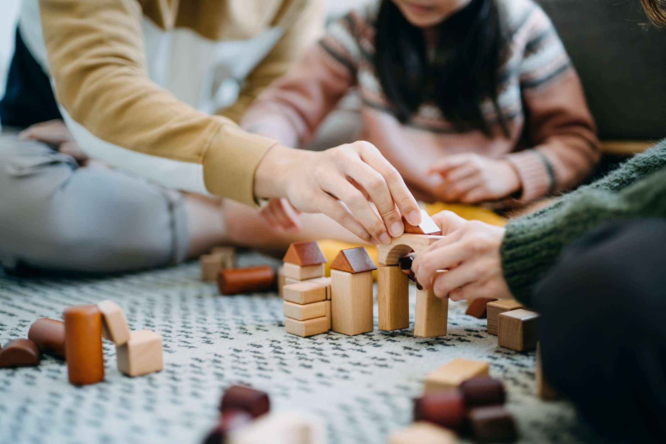 Nahaufnahme von fröhlichen asiatischen Eltern, die im Wohnzimmer auf dem Boden sitzen und Spaß haben und mit ihrer Tochter zusammen Holzbausteine spielen?