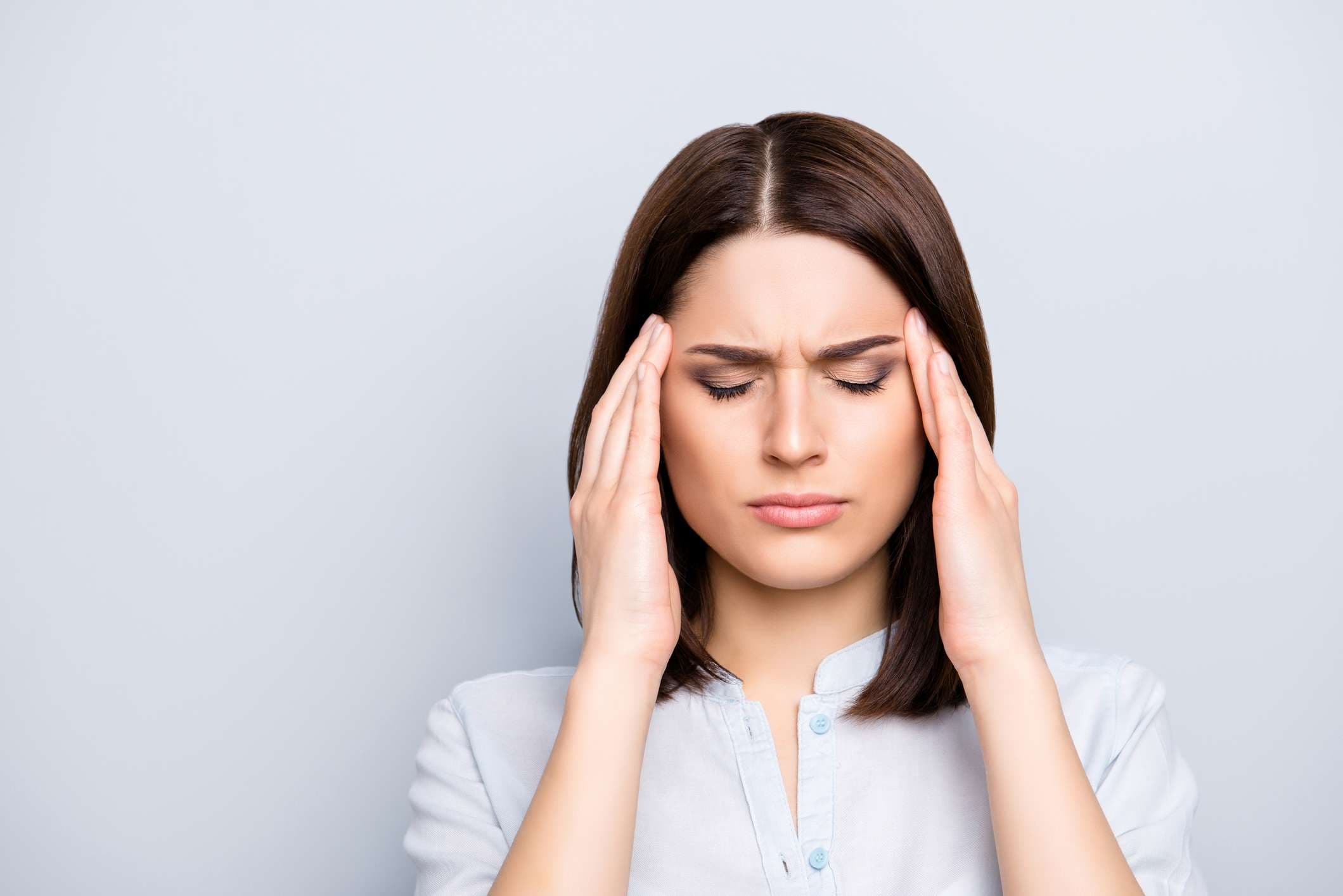 Porträt einer verärgerten, traurigen, hübschen, netten, charmanten, stilvollen Frau im Hemd, die Kopfschmerzen, Stress, Probleme hat, die Schläfen mit den Fingern und geschlossenen Augen berührt und auf grauem Hintergrund steht
