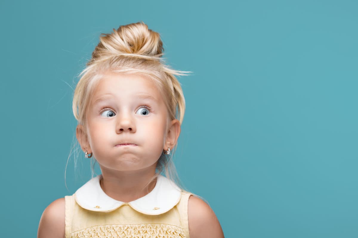 Small, young, funny girl, inflated cheeks on blue background