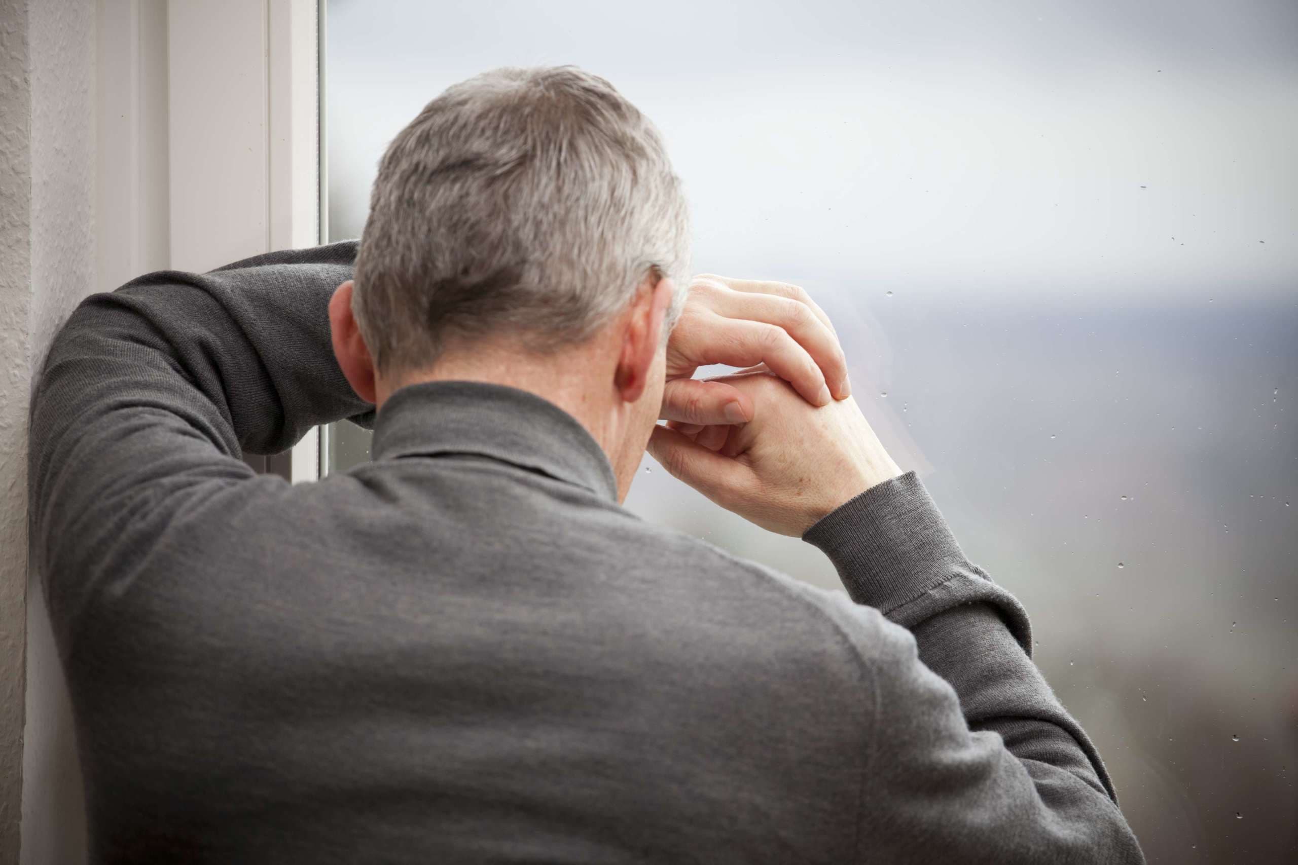 Trauriger reifer Mann, der sich mit Regentropfen an ein Fenster lehnt - konzentrieren Sie sich auf die Hände und das Fenster