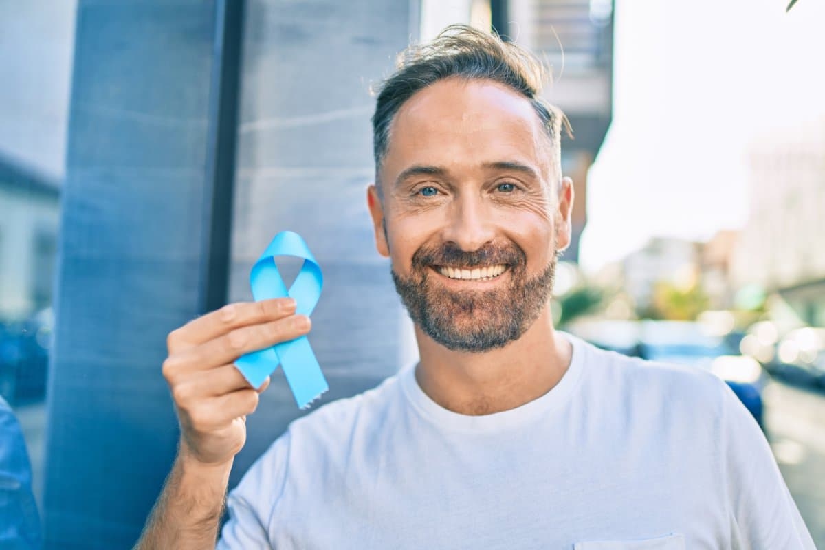 Middle age handsome man smiling happy holding blue prostate cancer ribbon at the city.