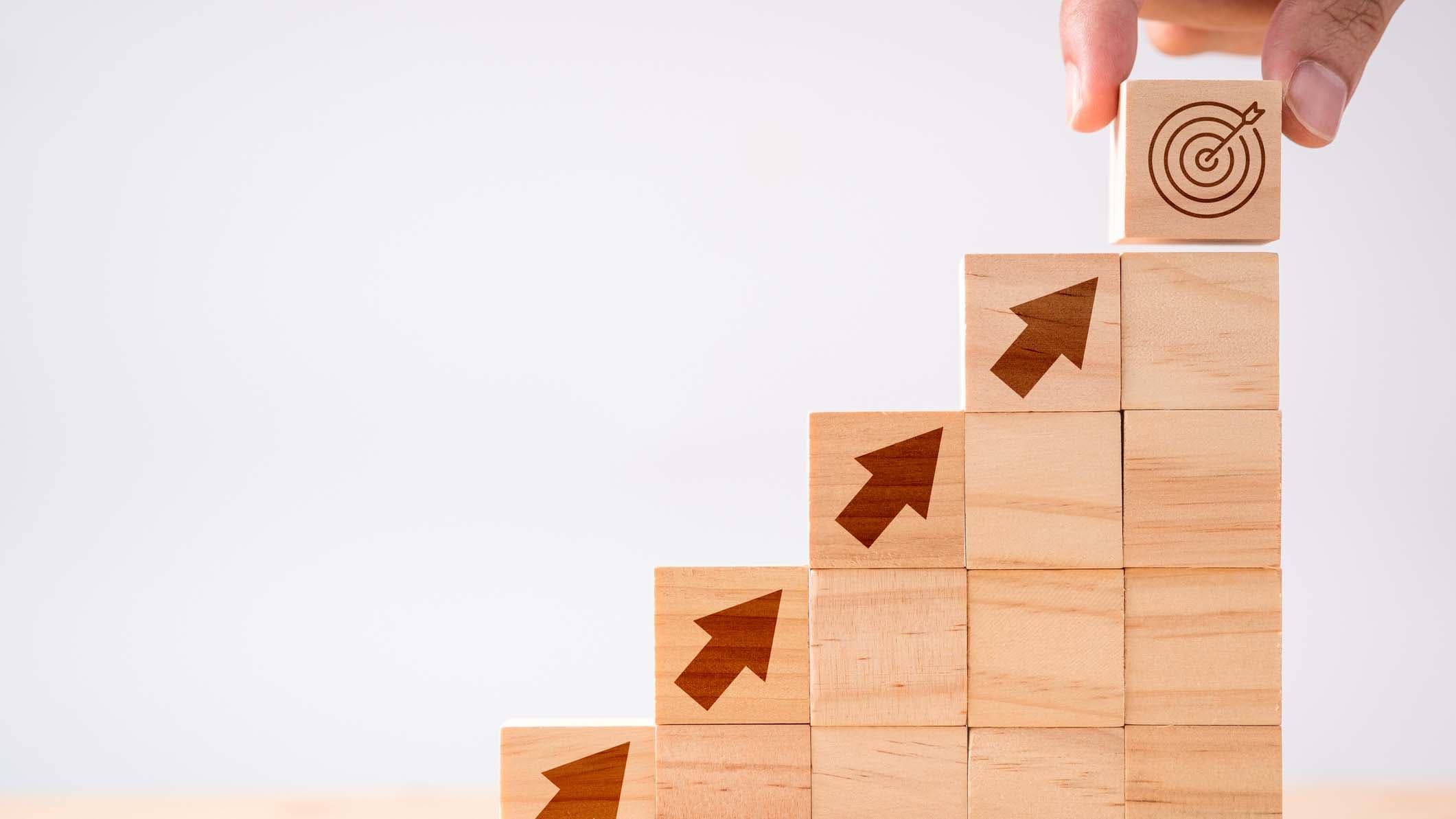 Hand, die den Druckbildschirmpfeil und den hölzernen Würfel der Zieltafel auf Pfeile nach oben setzt. Ziel der Investition und des Geschäftskonzepts.
