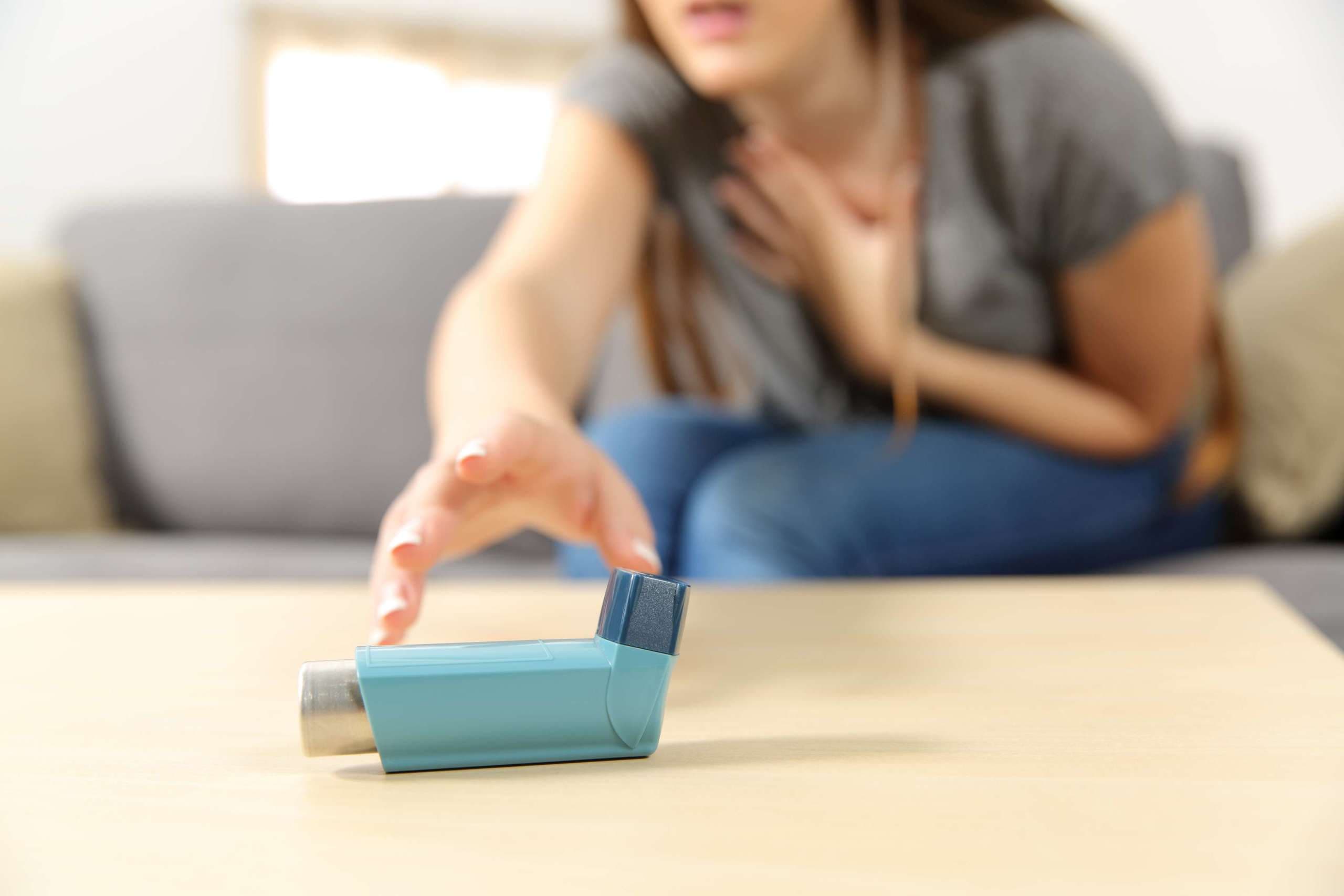Mädchen mit Asthmaanfall, der einen Inhalator auf einer Couch im Wohnzimmer zu Hause erreicht