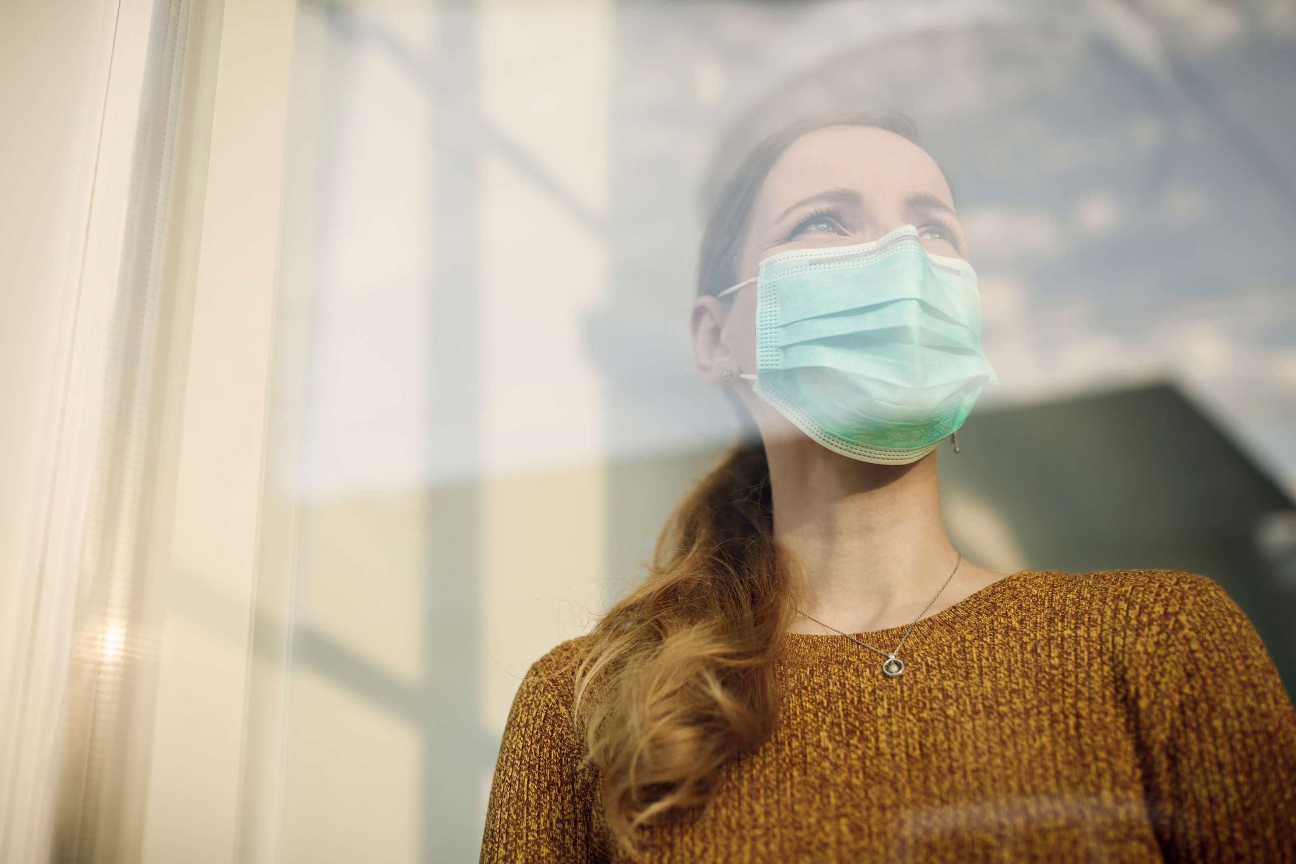 Niedrigwinkelansicht einer Frau, die eine schützende Gesichtsmaske trägt und durch das Fenster schaut. Platz kopieren.