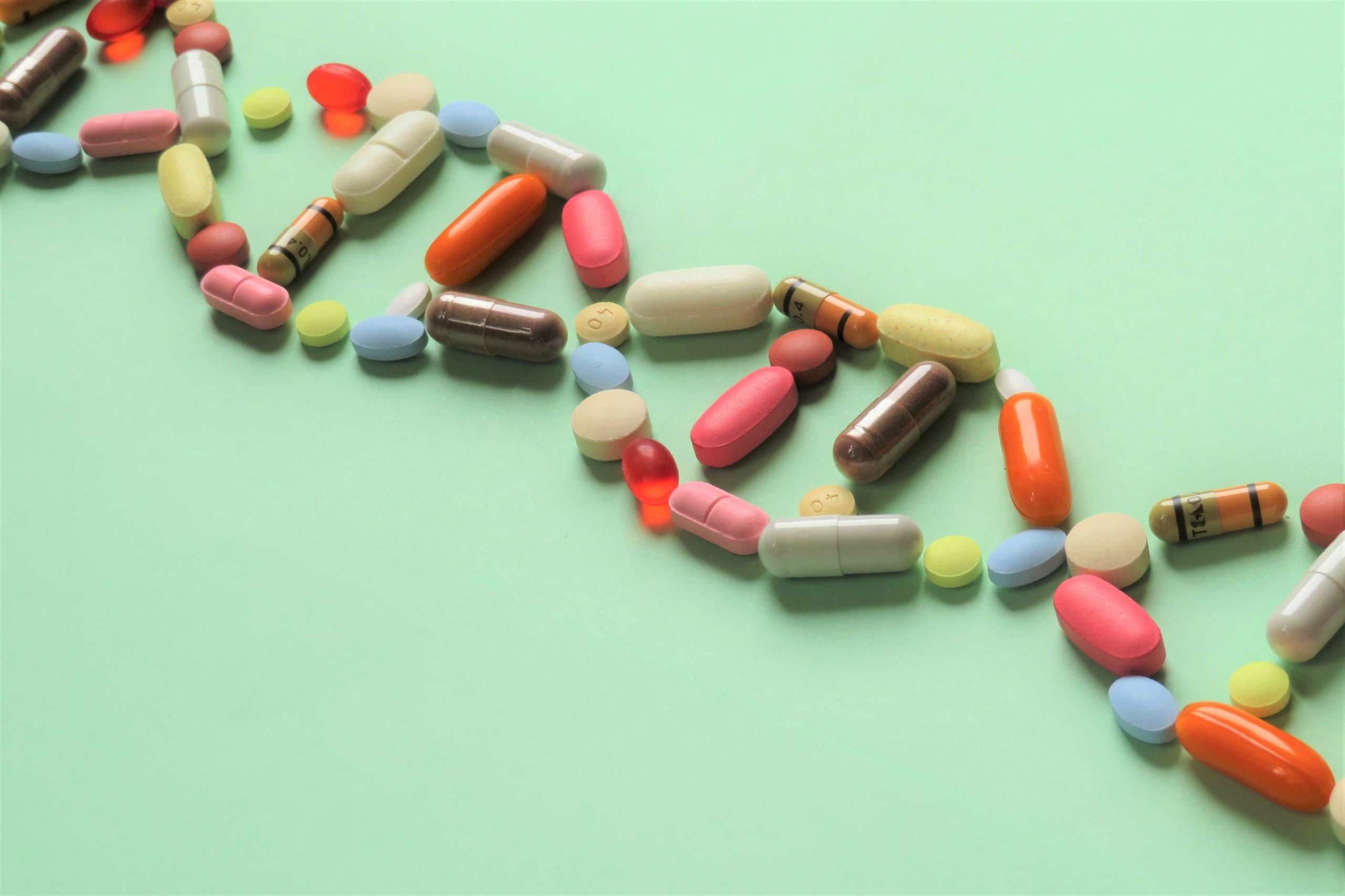 Horizontal image of prescription capsules and tablets of various shapes and colors arranged diagonally in the shape of DNA to represent pharmacogenetics.  Green background.