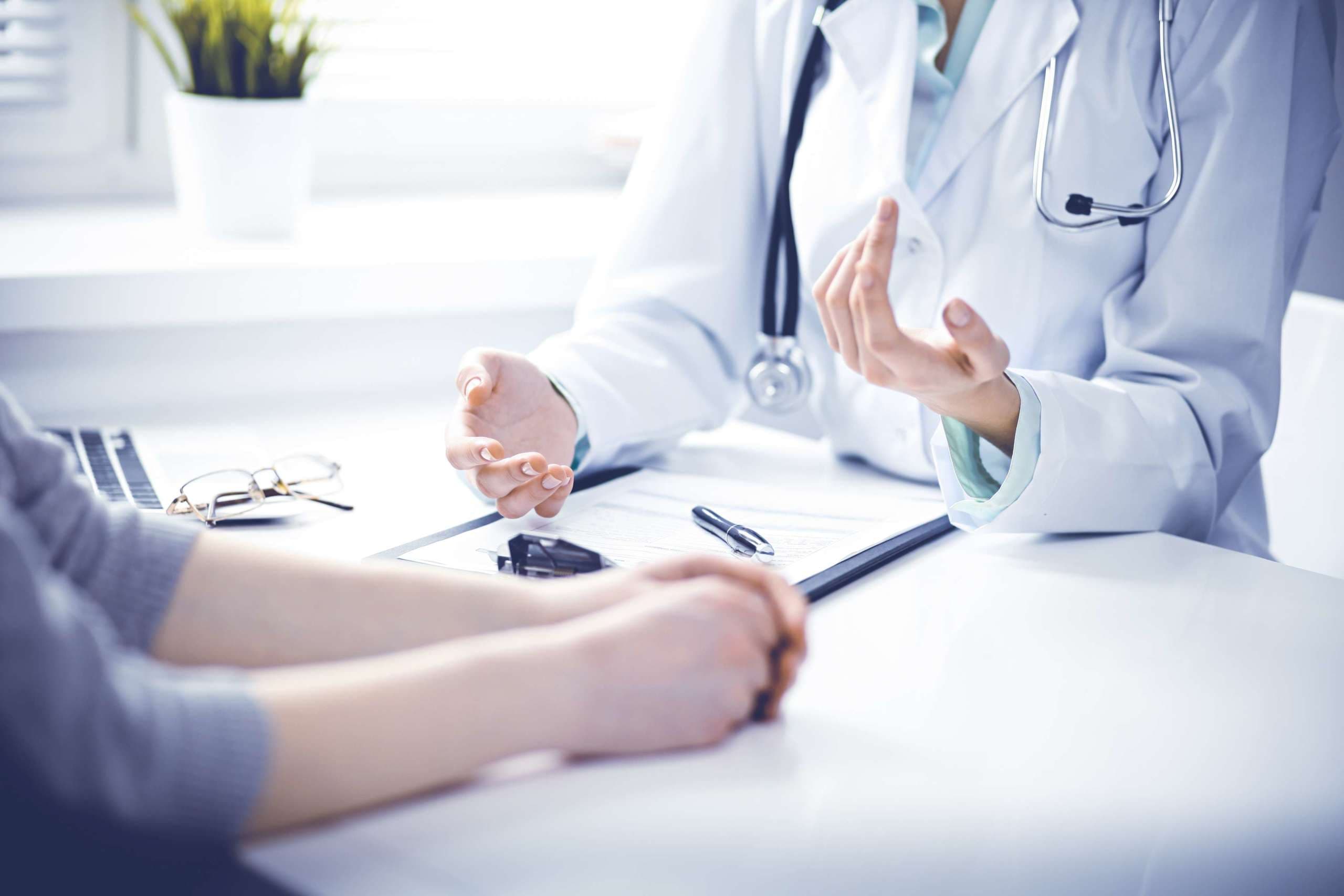 Nahaufnahme von Arzt und Patient, die am Schreibtisch in der Nähe des Fensters im Krankenhaus sitzen