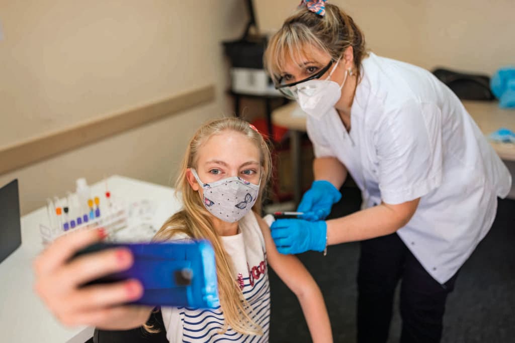 Mädchen, das Selfie macht, während sie von einer reifen weiblichen Gesundheitsfachkraft einen Coronavirus-Impfstoff erhält