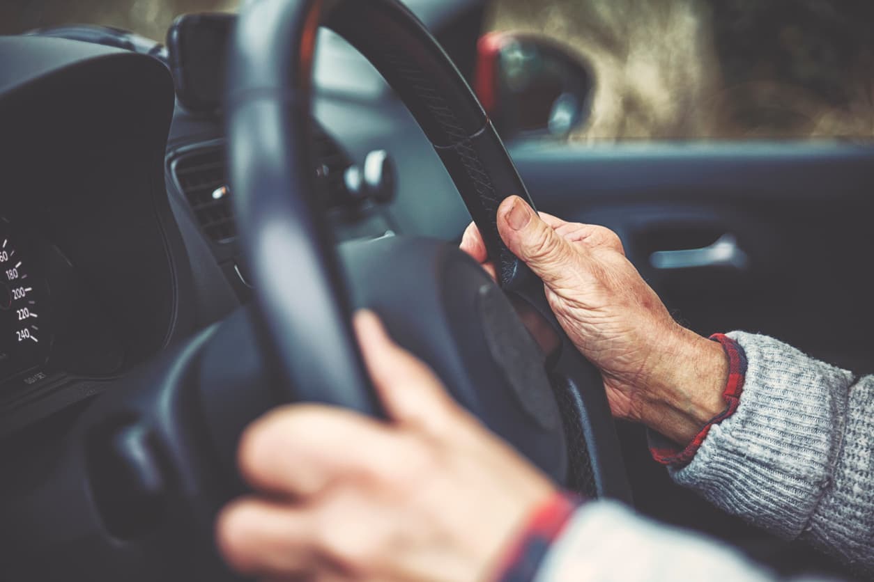 Hände einer alten Person am Lenkrad eines Auto