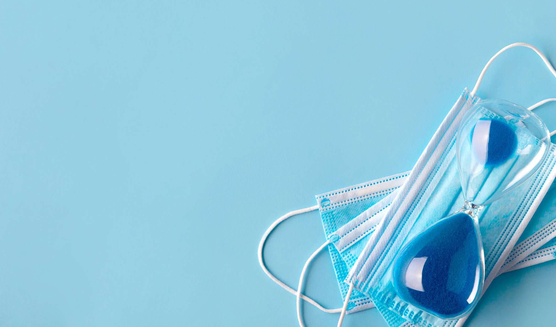 Sanduhr mit medizinischer Maske auf blauem Hintergrund. Ende des Quarantänekonzepts